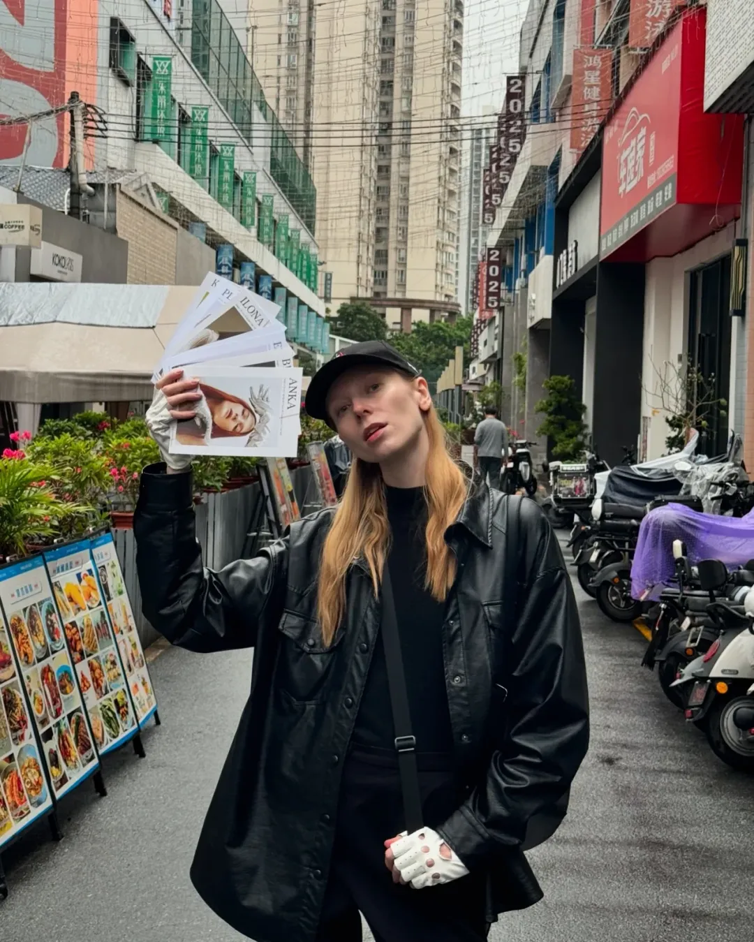 Model holding her comp cards on a city street in China, high-rise buildings and Chinese shop signs behind her