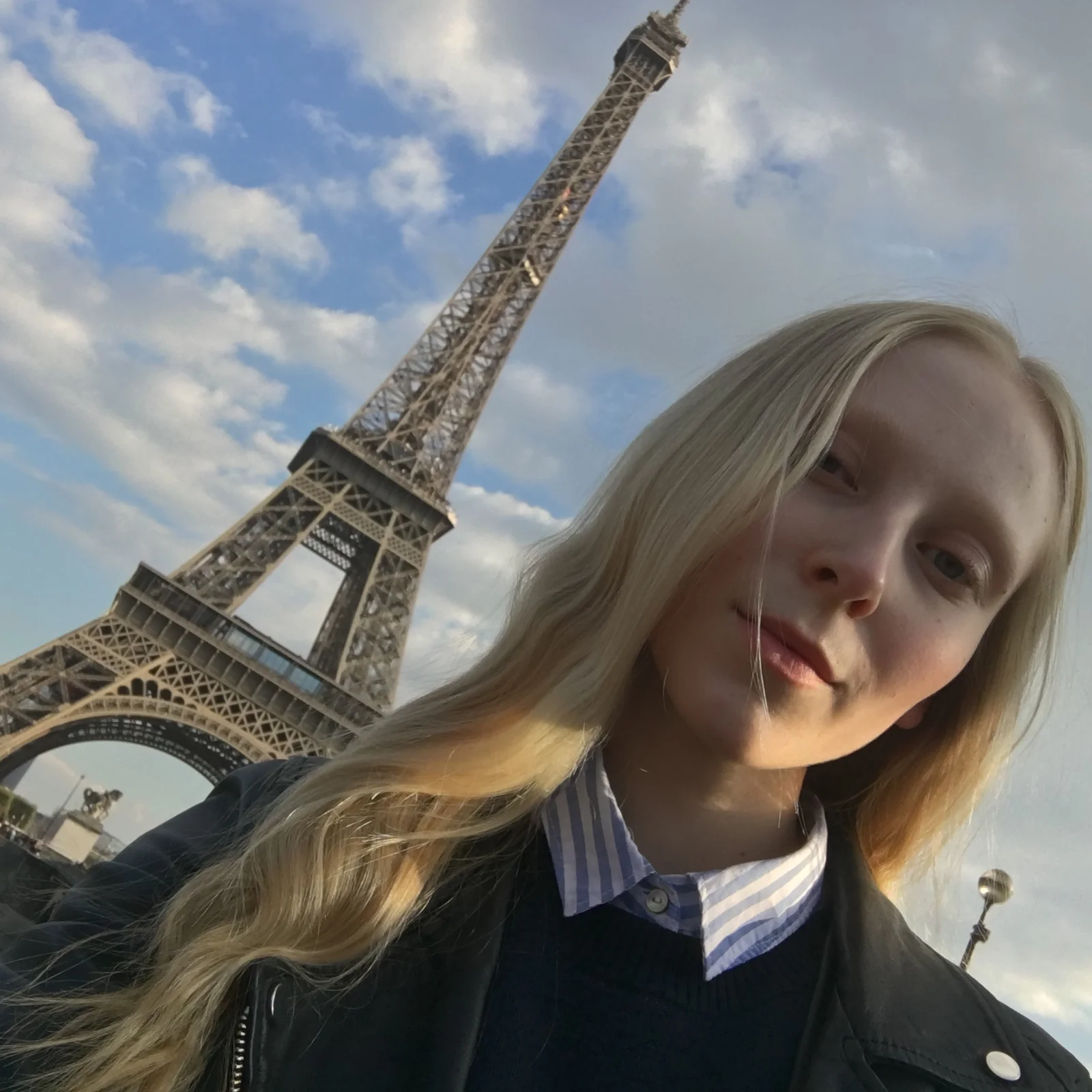 Model in a black leather jacket and striped shirt in front of the Eiffel Tower in Paris