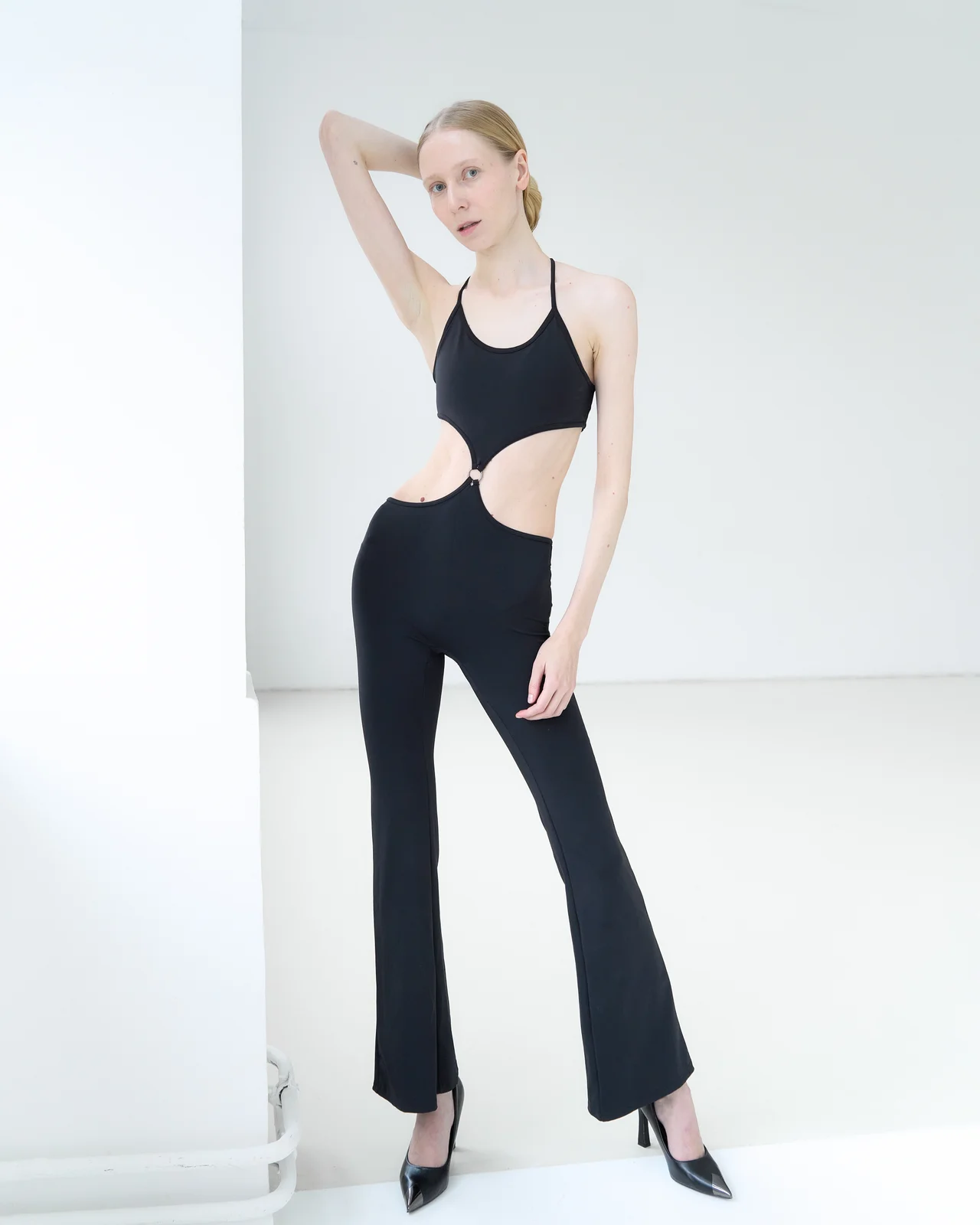 Model standing with one arm raised and her hand behind her head, the body stretched long