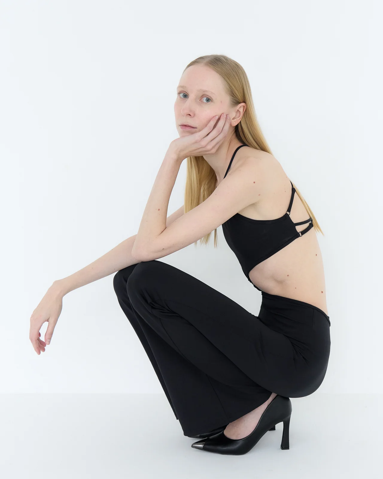 Model crouching with one hand resting softly against her cheek and the other relaxed over her knee