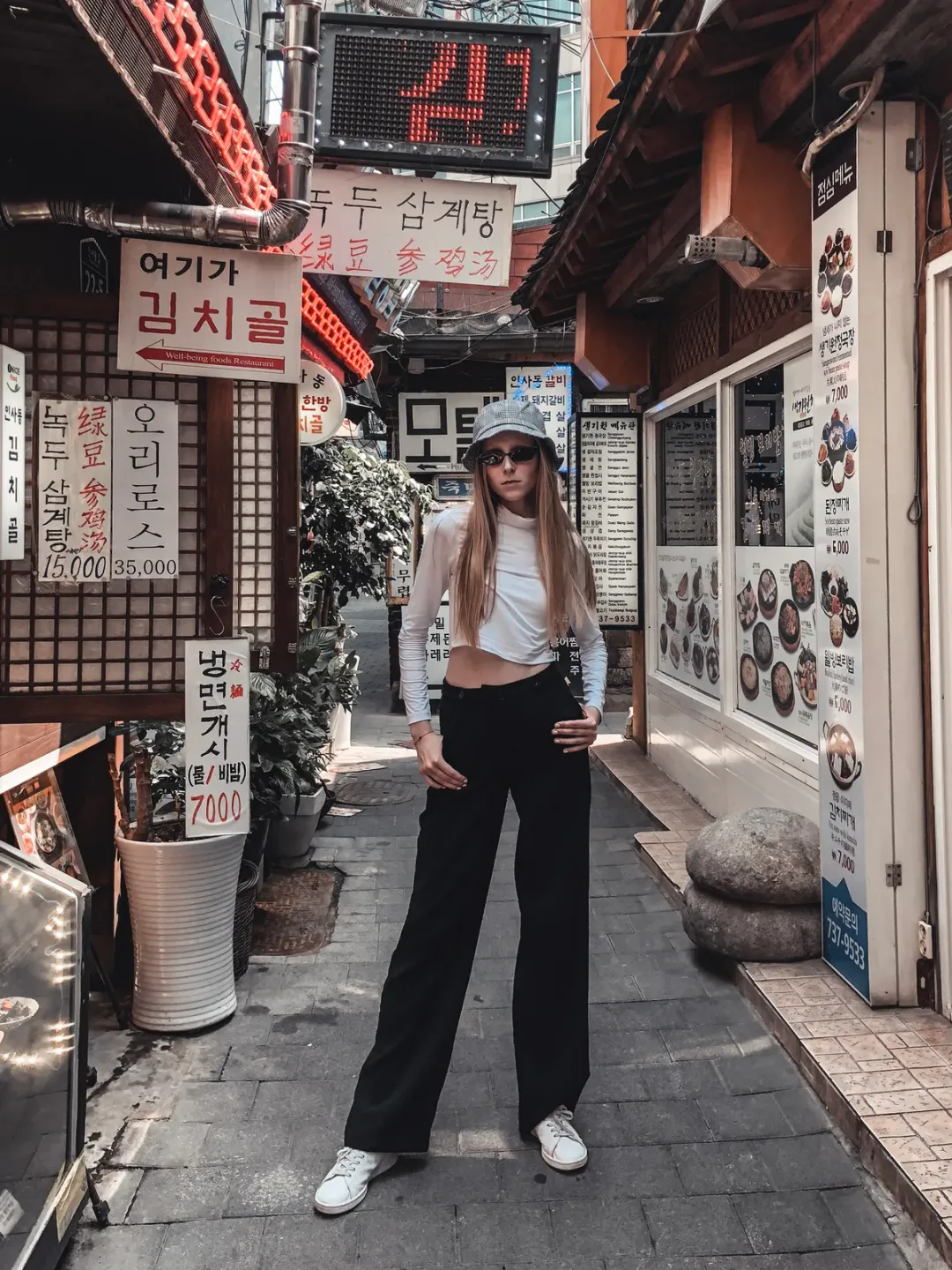 Model posing full-length in a narrow Seoul alley lined with Korean restaurant signs