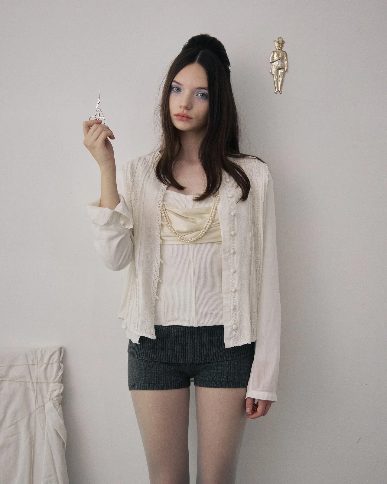 Ellie in a white blouse and long beaded necklaces, holding a small pair of scissors