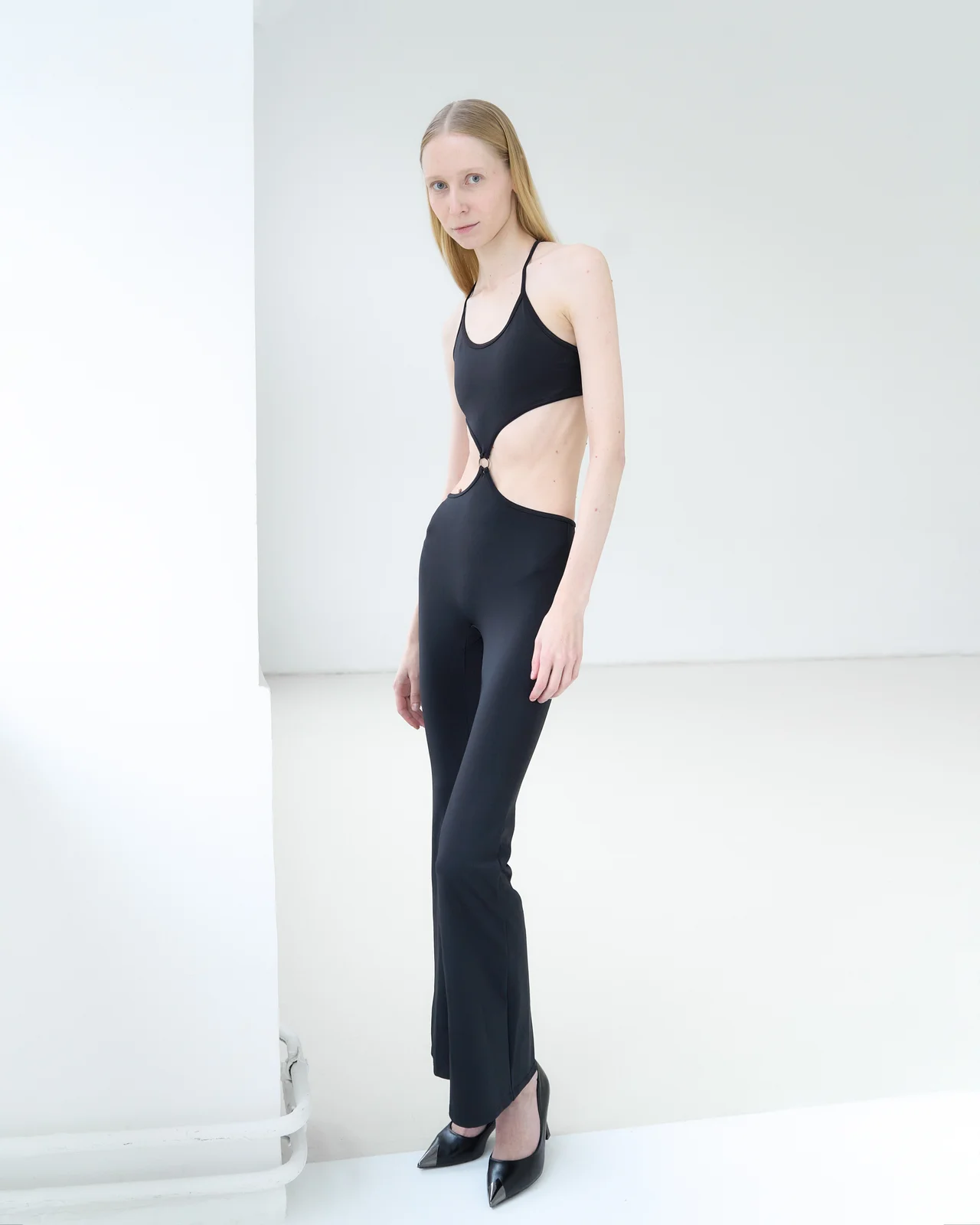 Model standing full-length in heels with her weight on one leg and the front foot pointed